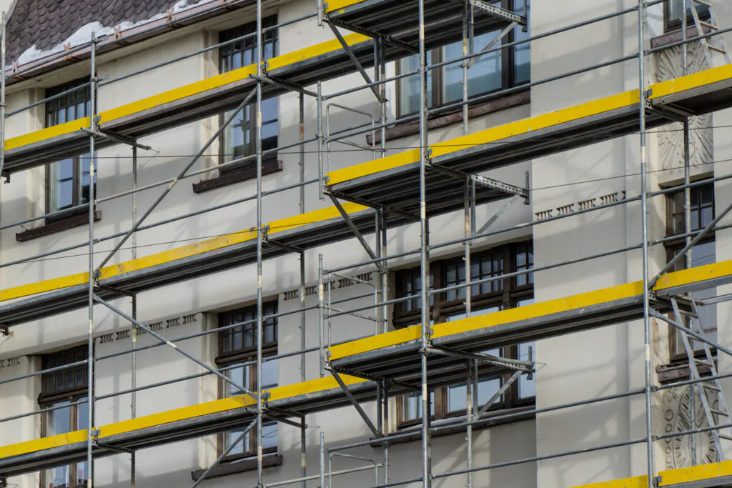 Industrial scaffolding grid with yellow walkways beside windows of old building, exterior repair project, temporary access structure for renovation