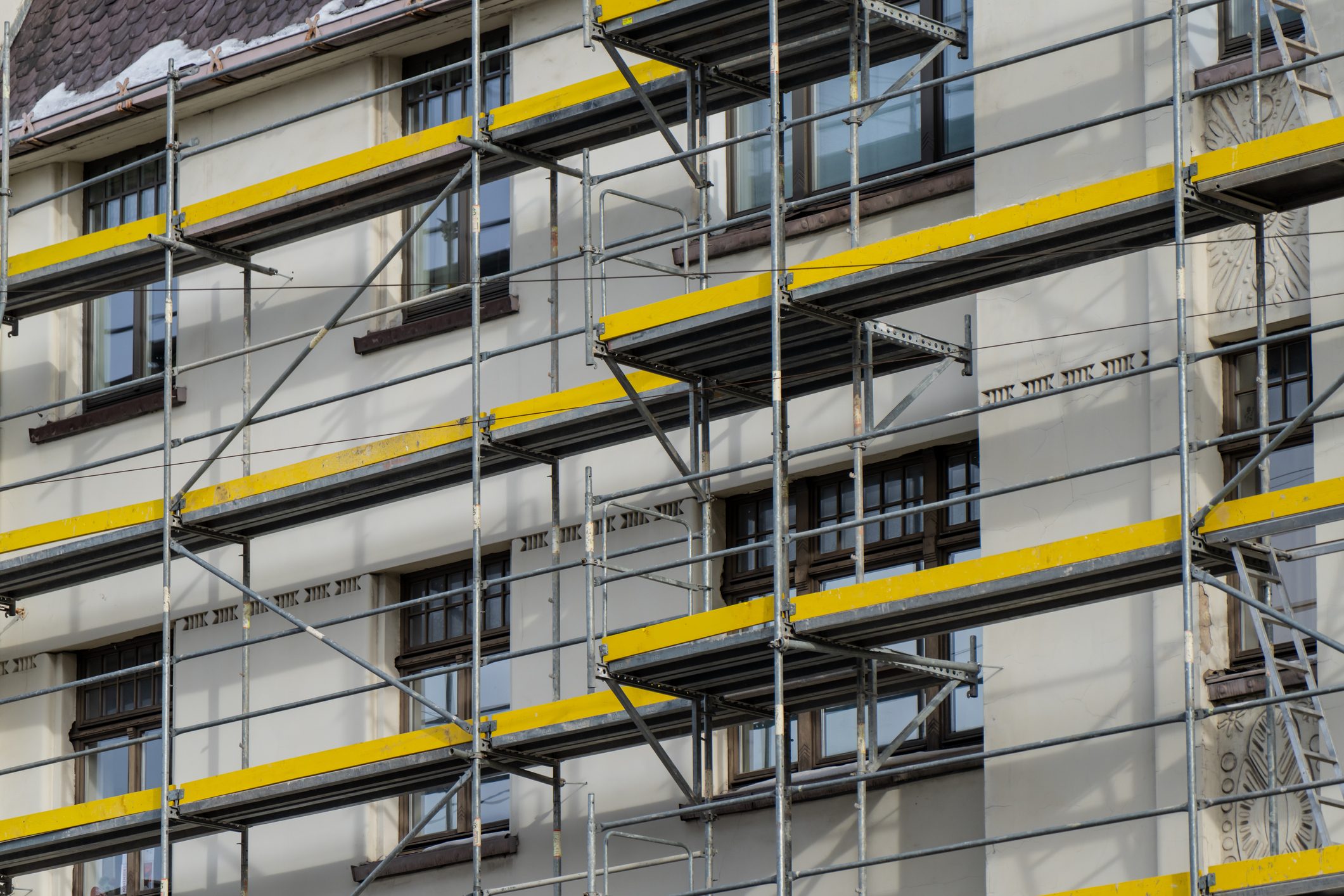 Industrial scaffolding grid with yellow walkways beside windows of old building, exterior repair project, temporary access structure for renovation